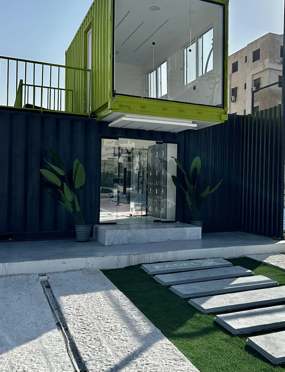 The Padel X clubhouse: a lime shipping container stacked over a dark entrance, with the courts behind it