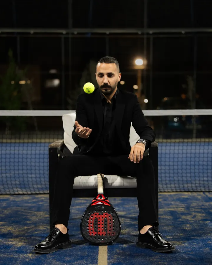 A player in a black suit sitting courtside with a racket